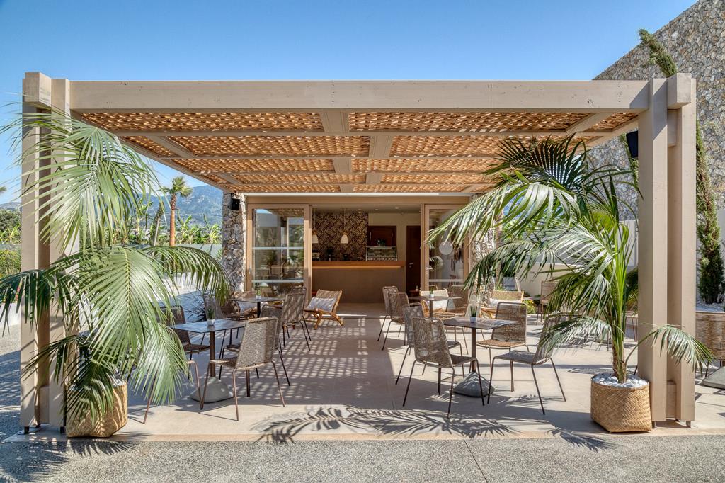Modern boho-stijl resort caf&eacute; met houten stoelen en tropische palmplanten op een luxe vakantiebestemming.